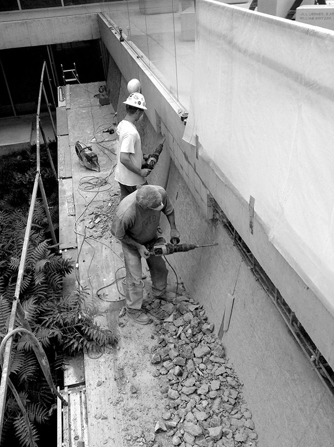 Workers on scaffold jackhammering the concrete fascia of the gallery.