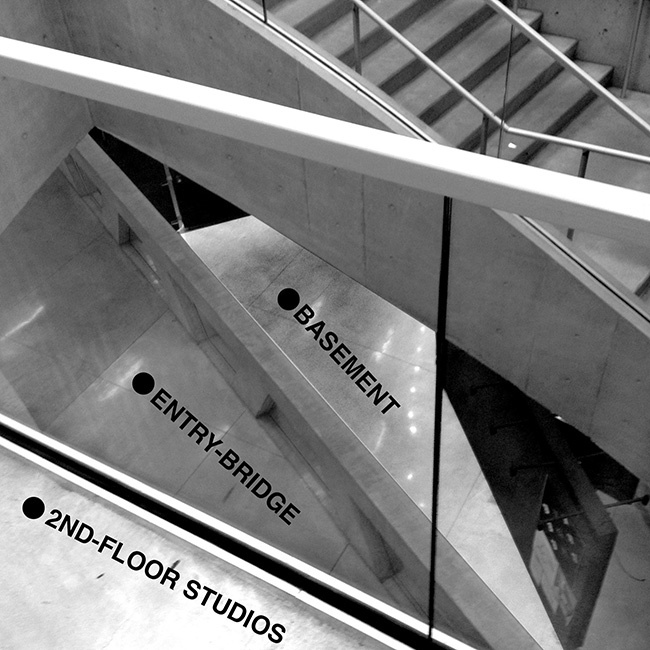 View looking down from Milstein Hall's second-floor, through the stair opening, at the ground-level bridge and basement Crit Room.